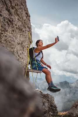 Klettersteig Dolomiten, Eggental: Frau auf Hängebank im Klettersteig, die mit dem Handy ein Selfie macht