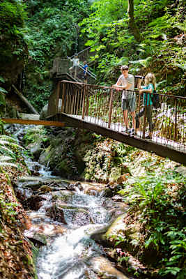 Stege führen durch die enge Rastenbachklamm, mehrere Personen sind auf dem Weg durch die Schlucht zu sehen.