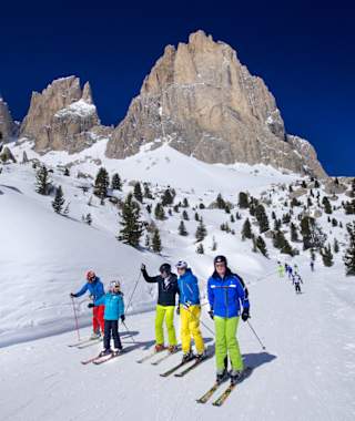 Fünf Skifahrer fahren die Sellaronda in Südtirol im Hintergrund ein schönes Dolomitenpanorama.