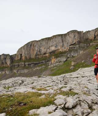 Vier Wanderer spazieren über ein Karstplateau, im Hintergrund ein formschöner Berg.