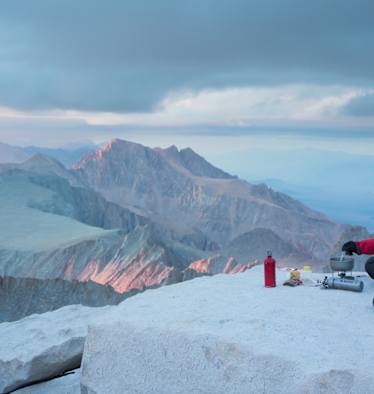 Mann kocht mit SOTO Kocher auf Berg Essen mit Panorama über Berge.