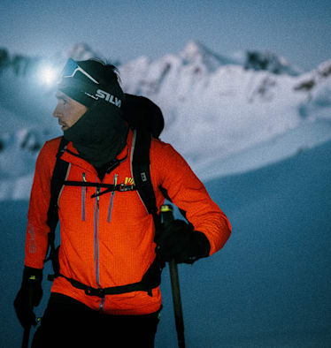 Ein Mann geht im Schnee und Skiausrüstung in der Nacht mit einer Stirnlampe skifahren.
