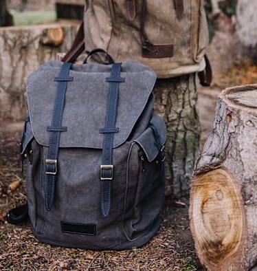 Der große Wanderrucksack von Servus in Grau in der Natur zwischen Baumstämme.