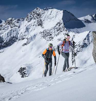 mann und frau beim skitouren gehen auf einem schneebedecktem berggipfel