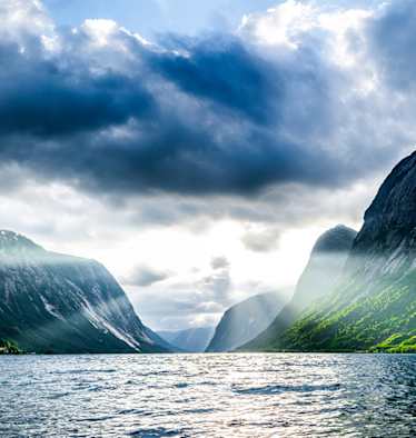 Norwegischer Fjord bei Sonnenaufgang mit schroffen Klippen und Wald 