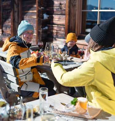 Zwei Damen stoßen mit einem Glas Wein auf der Skihütte im Winter an.