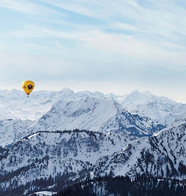 Ein gelber Heißluftballon, dahinter die schneebedeckten Alpen