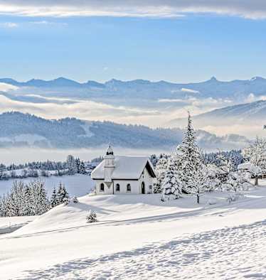 Die Hubertuskapelle in Scheidegg im Allgäu inmitten einer tief verschneiten Berglandschaft.