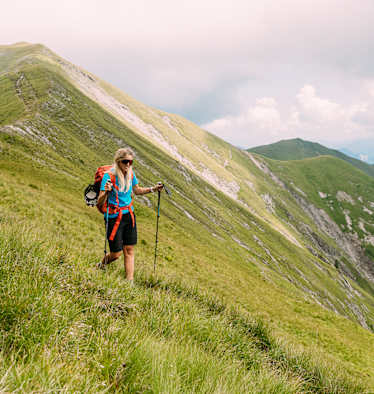 Wanderin geht mit Wanderstöcken über begrasten Berg