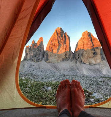 Ein Mann liegt in einem Zelt und genießt den Ausblick auf die Drei Zinnen.