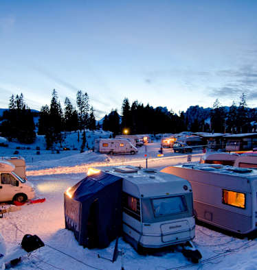 Der Wintercampingplatz Jaunpass bei Nacht. Es liegt Schnee und die Wohnwagen sind hell erleuchtet.