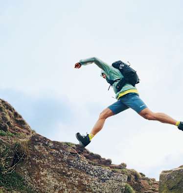Ein Mann trägt den neuen Remote Hike 23L von Berghaus und ist dabei von einer Stelle auf die andere zu springen.