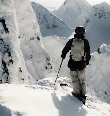 Ein Freerider steht auf einem Hang und blickt den verschneiten Berg hinab.