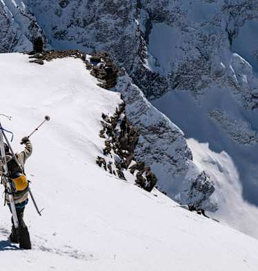 Auf einem schneebedeckten Hang stehen zwei Skitourengeher und zeigen in die Ferne. Sie sind mit der Bergtagen-Kollektion von Fjällräven ausgerüstet.