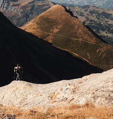 Ein Alpinist steigt einen Berg mit zwei Stöcken und der Haglöfs L.I.M ZT 2.0-Serie hinauf.