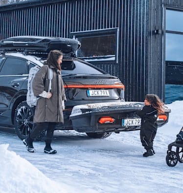 Eine vierköpfige Familie steht vor ihrem Auto, auf dem eine Thule-Heckbox befestigt ist.
