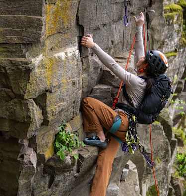 Eine Frau klettert auf einen Felsen mit dem neuen Gregory Rucksack Alpinisto 30.