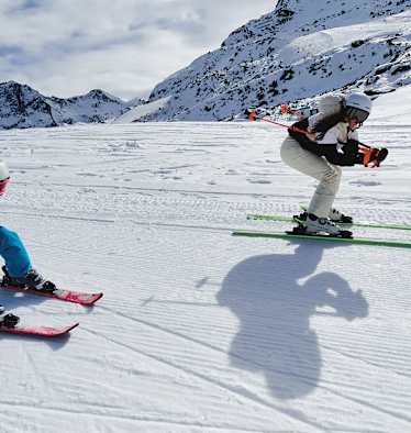 Eine Frau und ein Mädchen fahren gemeinsam Ski und nehmen dabei die Schussposition ein.