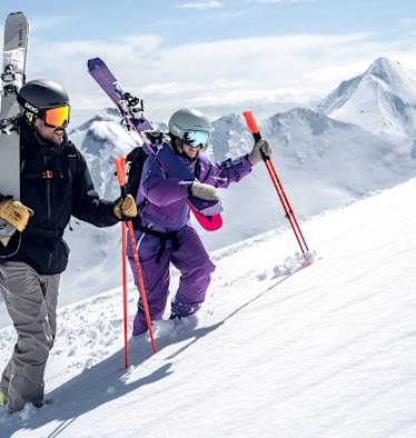 Ein Skifahrer und eine Skifahrerin gehen eine Piste in Ischgl hinauf.