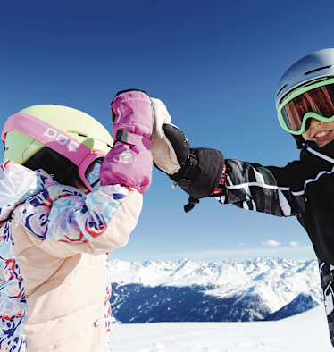 Ein Mädchen und ein Junge geben sich ein High Five. Hinter ihnen erstreckt sich das Bergpanorama von Kappl.