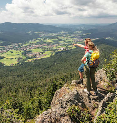 Eine Frau und ein Mann stehen auf einem Hügel und blicken auf die Wälder im Lamer Winkel.
