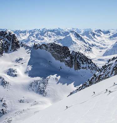 Markante Felsen die vom Schnee bedeckt sind. Skitourengeher fahren einen unverspurten Hang hinunter.