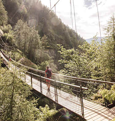 Eine Frau geht eine Hängebrücke in der Region Naturns entlang.