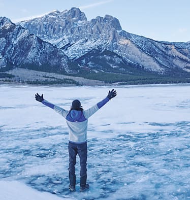 Ein Mann steht vor einem Berg im Schnee mit offenen Armen.