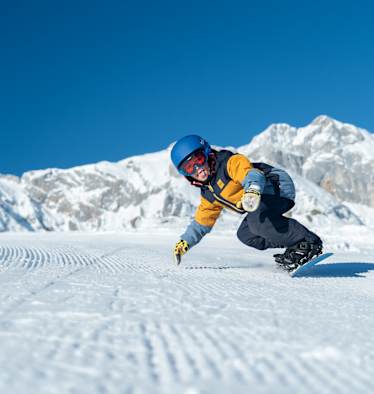 Ein Kind fährt in Snowboardbekleidung im Winter die Piste herunter.