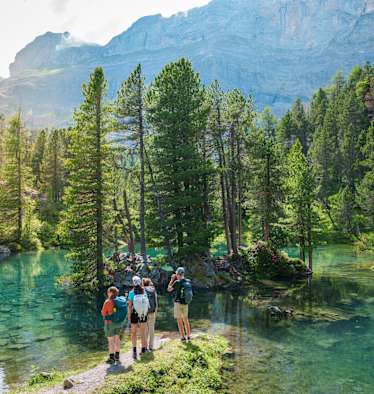 Vier Wanderer am Arvenseelo in der Schweiz, umgeben von Wasser und Wäldern.