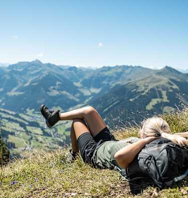 Wanderin liegt in der Wiese und genießt die Aussicht von der Gratlspitze im Alpbachtal in Tirol.