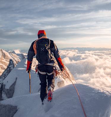 mann beim bergsteigen auf bergspitze, gekleidet in haglöfs