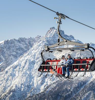 Ein Skilift in den verschneiten Bergen mit 2 Personen, die drinnen sitzen.