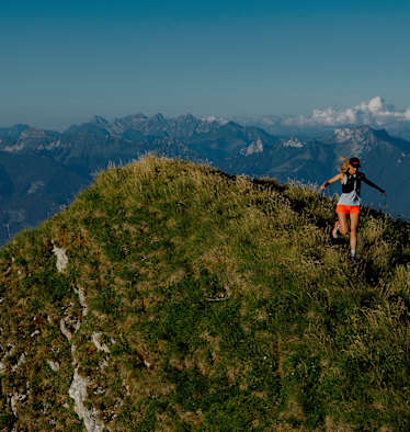 Eine Frau läuft auf einem Berg in einer alpinen, sommerlichen Kulisse.