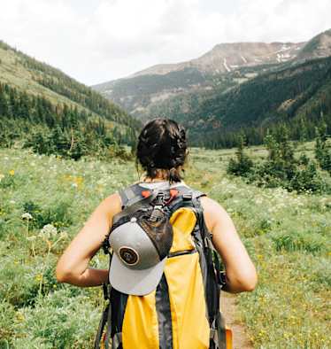 Eine Frau mit einem gelben Wanderrucksack spaziert durch eine bergige Landschaft.