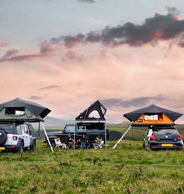 Zu sehen sind drei Autos auf einer Wiese auf denen drei unterschiedliche Tentbox Dachzelte montiert sind.