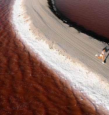 Eine Frau läuft einen sandigen Weg entlang inmitten eines braun-rötlichen Gewässers.