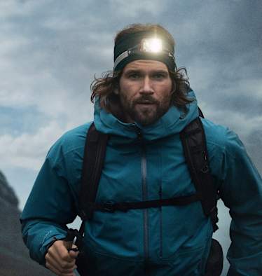 Ein Mann mit einer leuchten Stirnlampe geht mit Wanderausrüstung