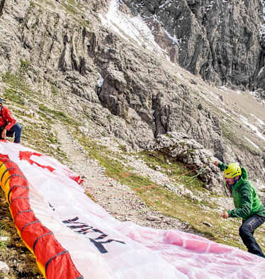 Der Tandemschirm wird vorbereitet, im Hintergrund ist eine mächtige Felswand zu sehen