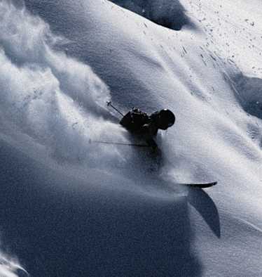 Skifahrer gleitet dynamisch durch unberührten Tiefschnee, wirbelt Pulverschnee auf und meistert eine steile Abfahrt in alpiner Winterlandschaft.