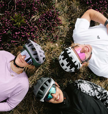 Drei junge Männer mit Helmen von Alpina liegen in der Wiese.