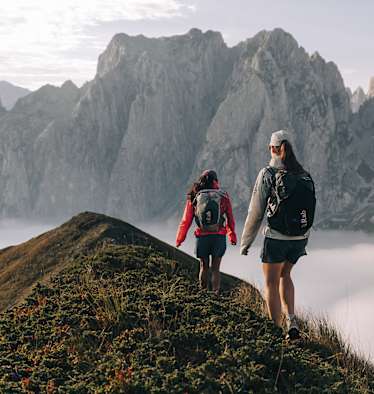 Zu sehen sind zwei Personen die einen felsigen Berg empor steigen und Rucksäcke von Rab tragen.