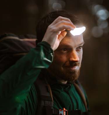 Mann ist in der Natur und benutzt eine Stirnlampe für gute Sicht.