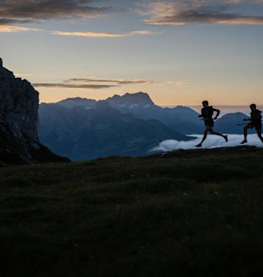 Zwei Trailrunner laufen im Morgengrauen am Berg.