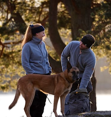 Ein Paar in Sportkleidung aus Merinowolle mit Schäferhund im Park im Herbst.