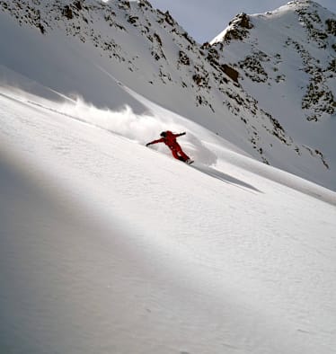 Eine Person fährt Snowboard im Schnee auf einem Berg in roter Ausrüstung.