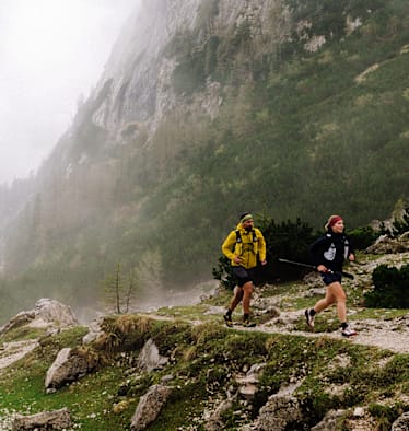 Zwei Läufer im Wald nahe eines Tals im Nebel.