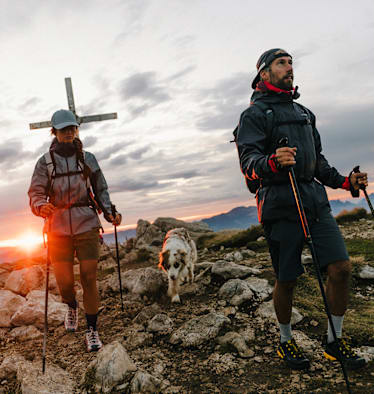 Ein Paar mit Hund wandert am Berg bekleidet mit Klediung von La Sportiva.