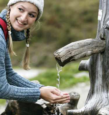 Wanderin schöpft Wasser aus einem Brunnen