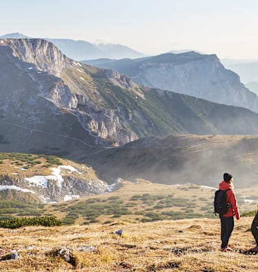 Zwei Wanderer stehen im Herbst auf dem Raxplateau und blicken in die Ferne